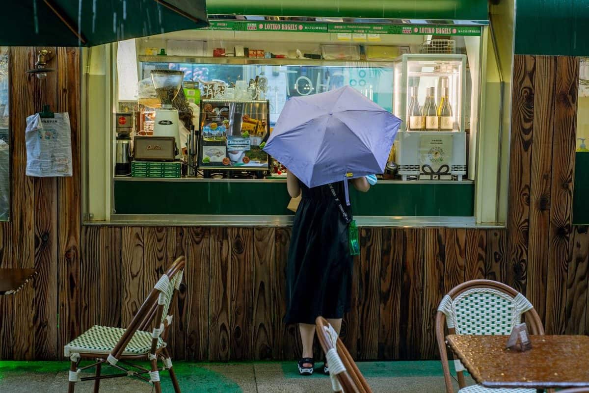 A person in a black dress holds a light purple umbrella at Lotiko's service window.