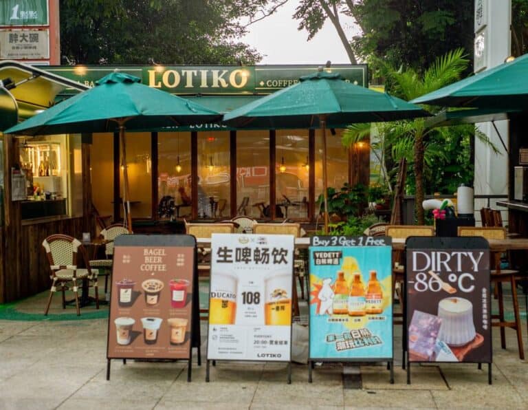 Outdoor patio at Lotiko with green umbrellas, wicker chairs, and four A-frame signs advertising drinks.