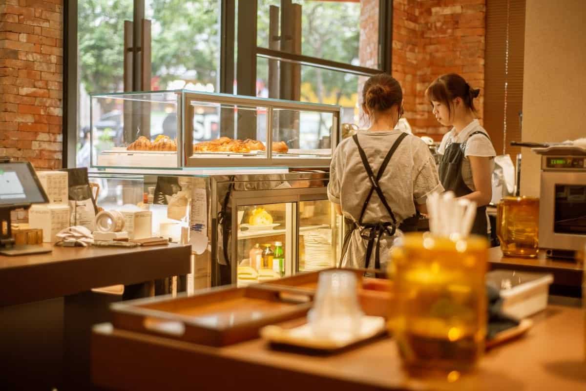 Two workers in aprons behind the counter at Walden's coffee with baked goods.