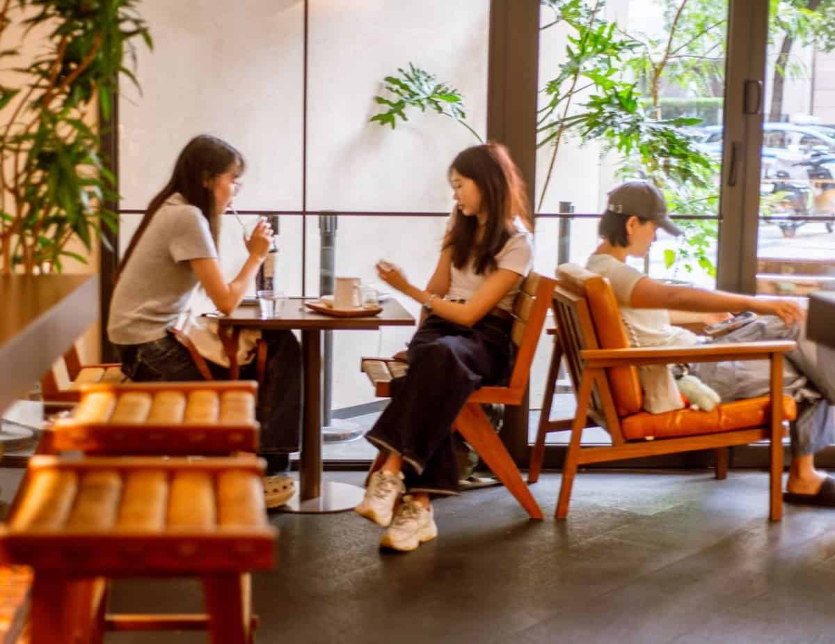 Two women and a person in a cap sit inside Walden's coffee near windows.