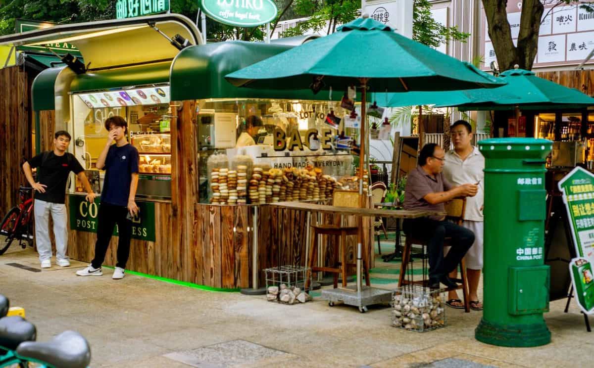 Lotiko food kiosk with men gathered outside, baked goods visible, and a green China Post mailbox in the foreground.