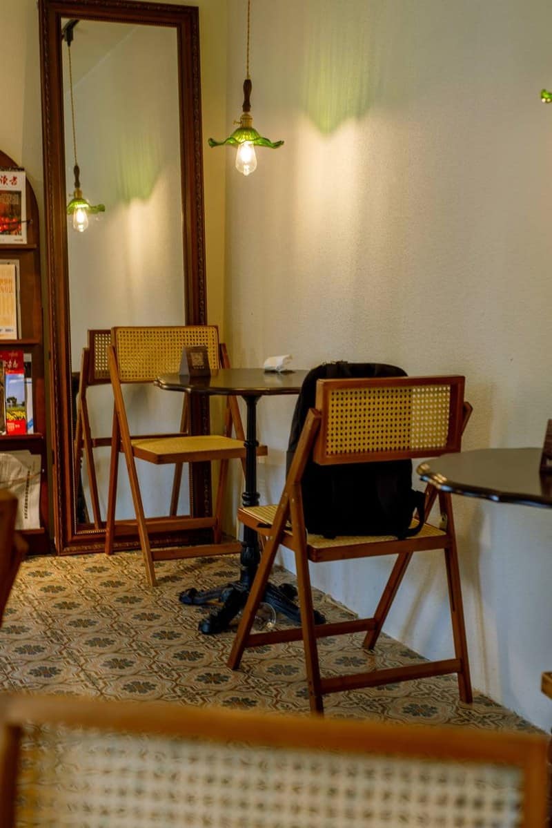 Lotiko dining area with cane-seat chairs, dark tables, and a black bag beneath a green shade.