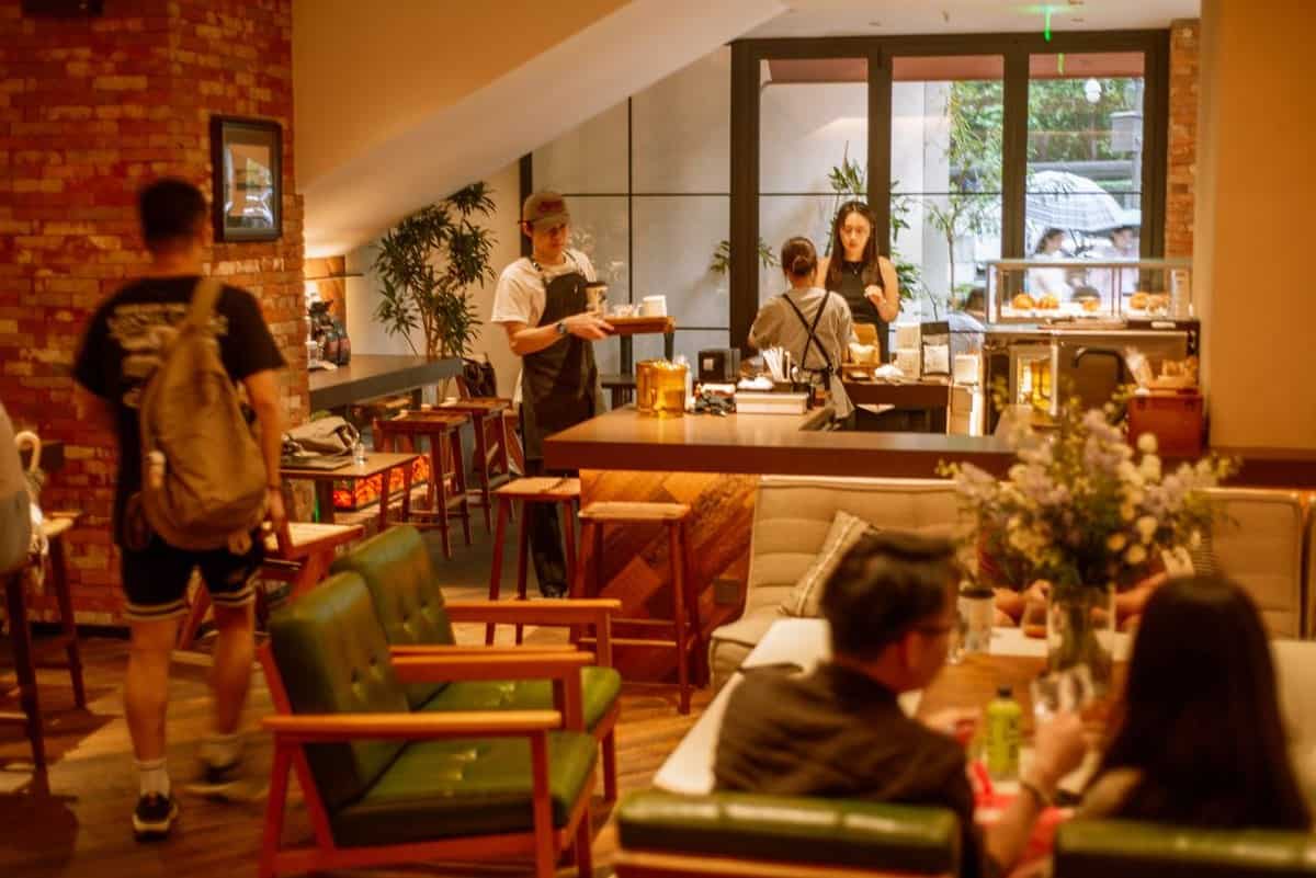 Interior of Walden's coffee with exposed brick walls, green seating, and a server carrying a tray near the counter.