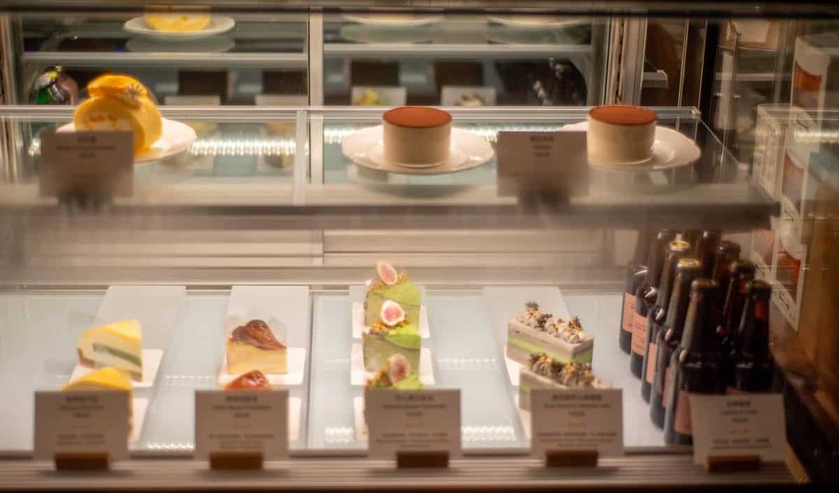 Glass display case at Walden's coffee holds whole cakes, sliced pastries, and dark bottles under warm light.