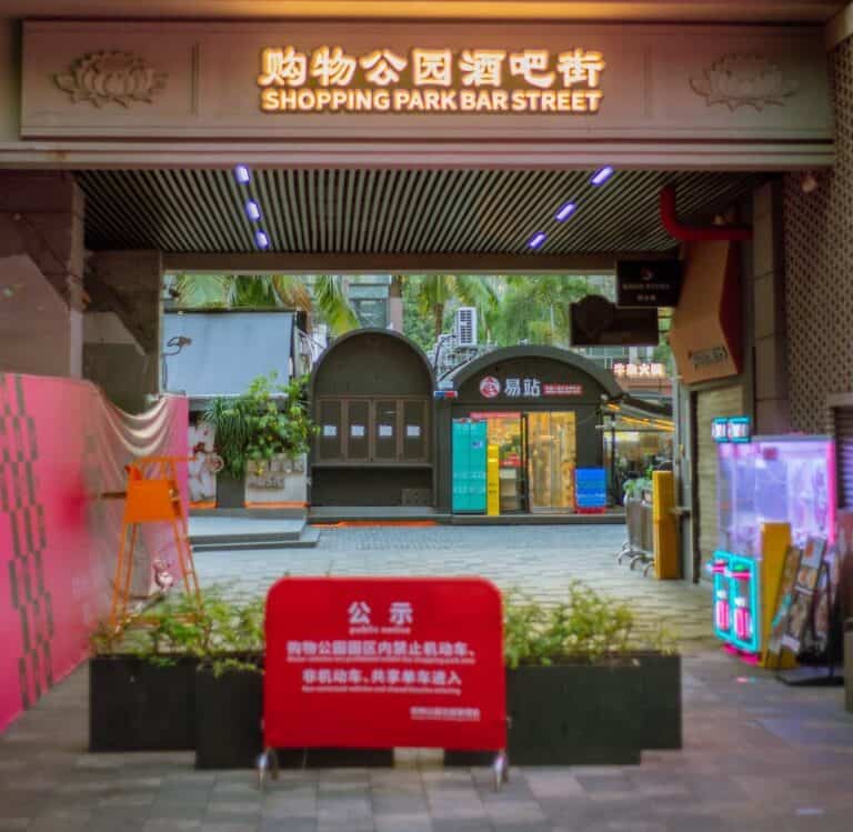 Covered entrance to Coco Park with a bilingual overhead sign and a red Chinese prohibition notice in the foreground — thirstyguide.com