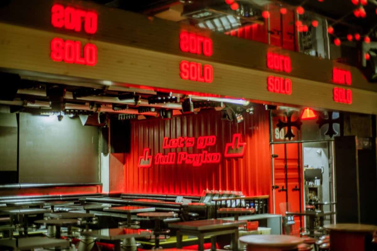 Coco Park interior with wooden tables, red SOLO neon signs, and a corrugated wall reading Let's go full Psyko — thirstyguide.com