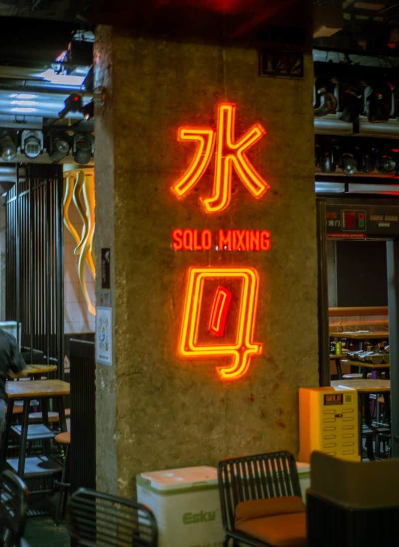 Red-orange neon sign at Coco Park displays 水, “SOLO MIXING,” and a glass outline near tables and a white esky — thirstyguide.com