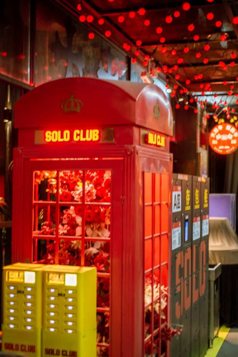 Red Solo Club booth with signage and artificial flowers beside yellow power-bank stations and lockers at Coco Park — thirstyguide.com