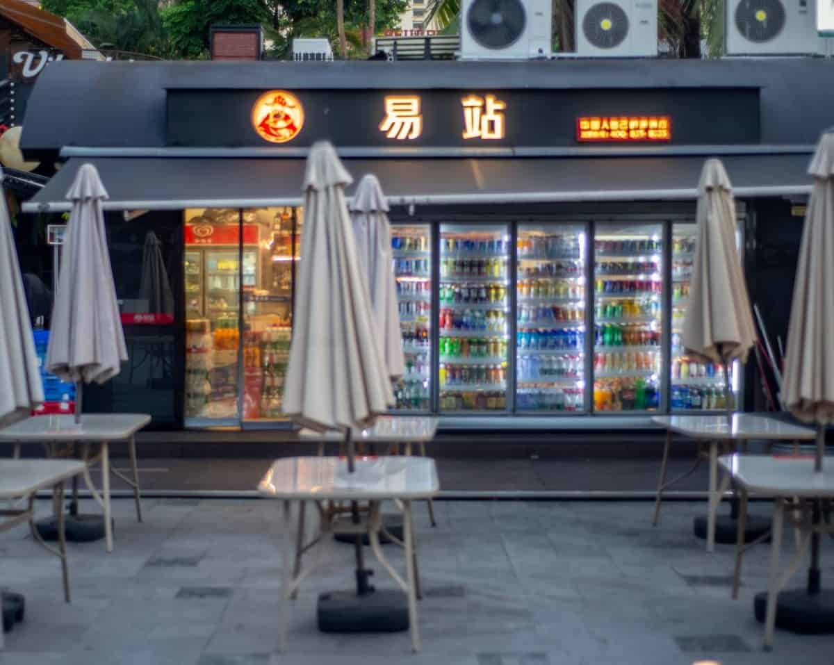 Coco Park exterior with illuminated Chinese signage, refrigerated drinks visible through windows, and empty white tables — thirstyguide.com