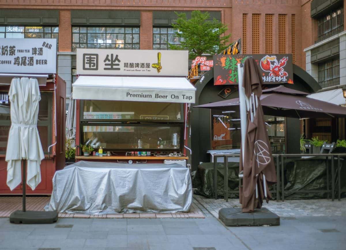 Coco Park covered tables and folded umbrellas in front of storefronts including a beer bar — thirstyguide.com