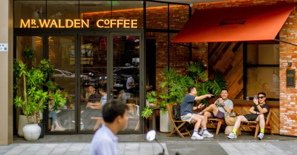 Walden's coffee exterior with three men seated under an orange awning and a motor scooter passing in the foreground.