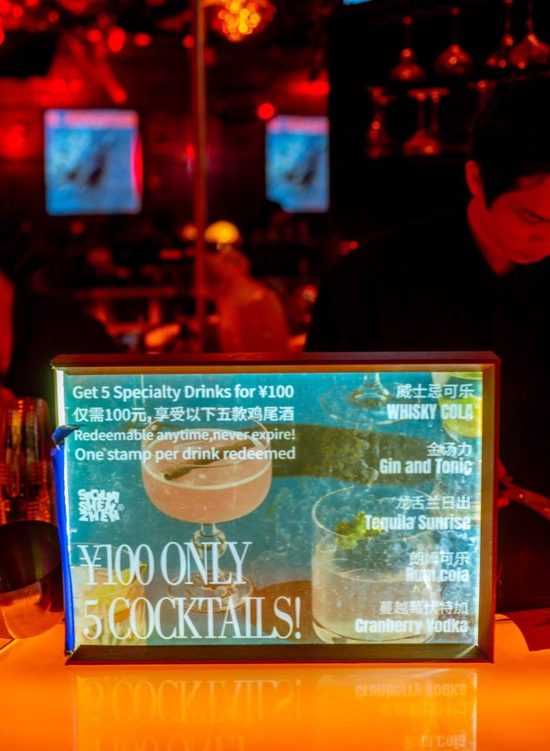 Backlit cocktail sign at Scillia and Solo bar, blurred figures in red light — thirstyguide.com