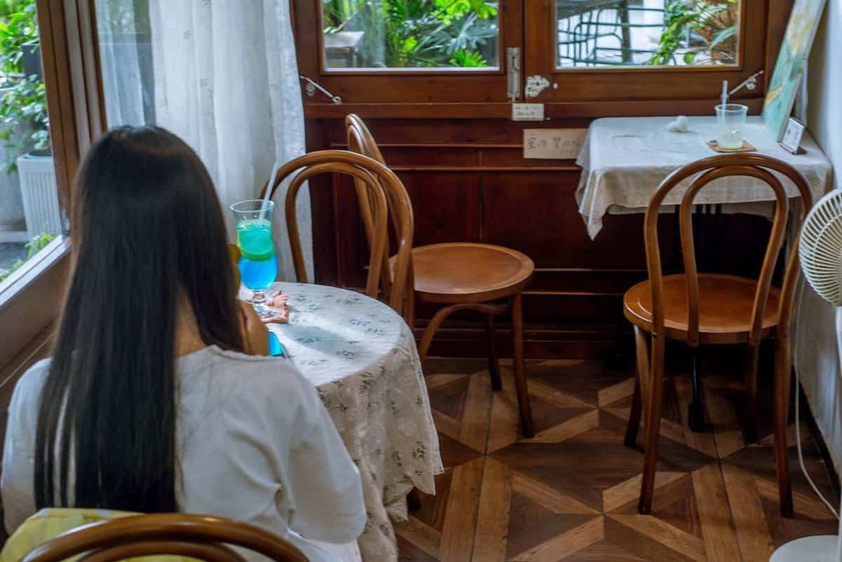 A woman sits at a lace-covered table with a blue-green drink at Moon Ke Coffee (Moon可咖啡), Shenzhen — thirstyguide.com