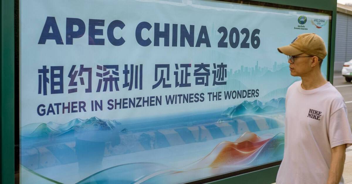Man by an APEC CHINA 2026 billboard for 30 Things to Do Before You Come to Shenzhen, China for APEC 2026 — thirstyguide.com