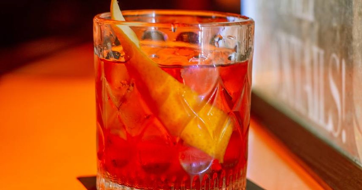 A cut-glass tumbler with a red-orange drink on an orange counter at Scillia and Solo bar, photographed for thirstyguide.com